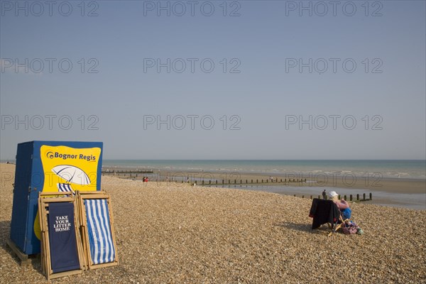 ENGLAND, West Sussex, Bognor Regis, Deck chair hire station on sand and shingle beach with a woman sitting on a chair looking out towards the sea