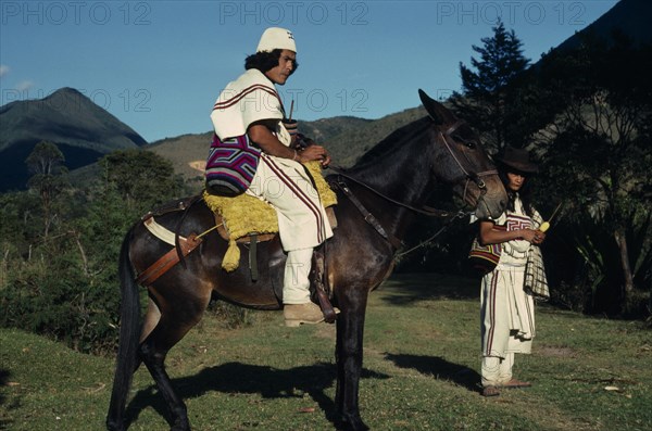 COLOMBIA, Sierra Nevada de Santa Marta, Ika, Ika leader Vicente Villafana on mule with another man standing at his side  both in traditional dress of woven wool&cotton mantas cloaks  mochilas shoulder carrying bags. Vicente wears a woven cactus fibre helmet.  Arhuaco Aruaco indigenous tribe American Colombian Colombia Hispanic Indegent Latin America Latino Male Men Guy Scenic South America  Arhuaco Aruaco indigenous tribe American Colombian Columbia Hispanic Indegent Latin America Latino Male Men Guy Scenic South America Male Man Guy Classic Classical Fiber Historical Older