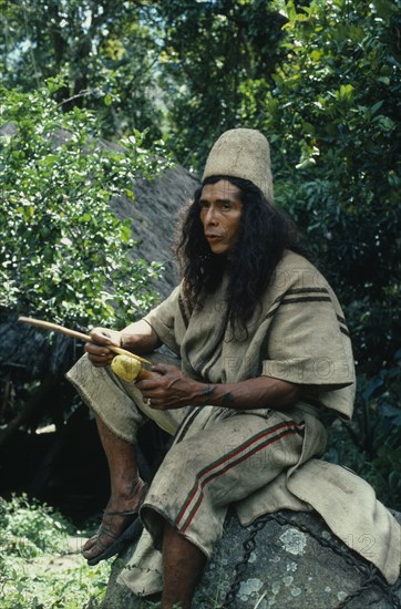 COLOMBIA, Sierra Nevada de Santa Marta, Ika, Ika man in traditional dress  helmet of woven cactus fibre  hand woven wool&cotton manta cloak and trousers.Holds his poporo small gourd containing powdered lime. He inserts the powdered lime into a wad of coca leaves held in the cheek  then rubs the neck of the gourd with the palito small stick forming an ever growing lime encrustation. This activity has a religo-sexual significance and deadens the pangs of hunger and cold. Arhuaco Aruaco indigenous tribe American Classic Classical Colombian Colombia Hispanic Historical Indegent Latin America Latino Male Men Guy Older South America  Arhuaco Aruaco indigenous tribe American Classic Classical Colombian Columbia Hispanic Historical Indegent Latin America Latino Male Men Guy Older South America History Male Man Guy One individual Solo Lone Solitary 1 Fiber Single unitary