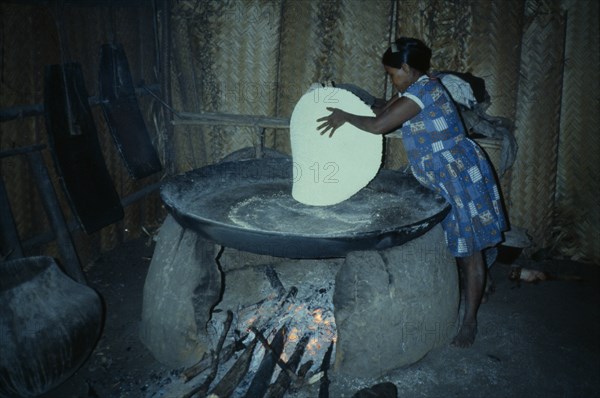 COLOMBIA, North West Amazon, Tukano Indigenous People, Barasana woman making casabe bread from manioc flour baked on large circular shallow clay oven over wood fire enclosed by clay oven wall.  Tukano sedentary Indian tribe North Western Amazonia cassava American Colombian Columbia Female Women Girl Lady Hispanic Indegent Latin America Latino South America Tukano Female Woman Girl Lady One individual Solo Lone Solitary