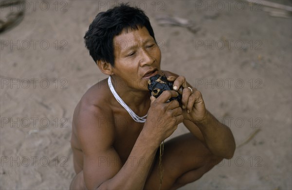 COLOMBIA, North West Amazon, Tukano Indigenous People, Barasana shaman playing deer skull flute outside the maloca/large communal home. Tukano sedentary Indian tribe North Western Amazonia American Colombian Columbia Hispanic Indegent Latin America Latino Religion South America Tukano One individual Solo Lone Solitary Religious