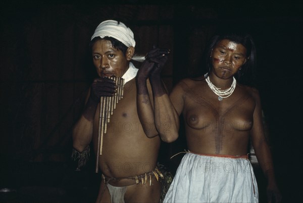 COLOMBIA, North West Amazon, Tukano Indigenous People, Group of young Barasana dancing a panpipe dance inside maloca/communal home - their bodies and faces painted with red Achiote for ceremonial manioc festival. Tukano sedentary Indian tribe North Western Amazonia American Colombian Columbia Female Women Girl Lady Hispanic Indegent Latin America Latino South America Tukano Female Woman Girl Lady Immature