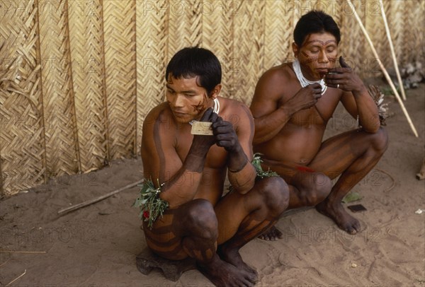 COLOMBIA, North West Amazon, Tukano Indigenous People, Barasana men applying dark red Achiote (from fruit seeds) facial paint  also apply dark purple we dye from boiled leaves of forest liana in  geometric designs over legs arms and hands. Tukano sedentary Indian tribe North Western Amazonia body decoration American Colombian Columbia Hispanic Indegent Latin America Latino Male Man Guy South America Tukano Male Men Guy
