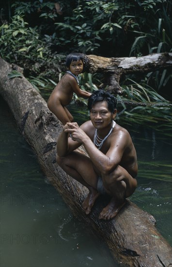 COLOMBIA, North West Amazon, Tukano Indigenous People, Barasana father Pacico and his son stand on log at river port.  Tukano sedentary Indian tribe North Western Amazonia family American Colombian Columbia Dad Hispanic Indegent Kids Latin America Latino South America Tukano