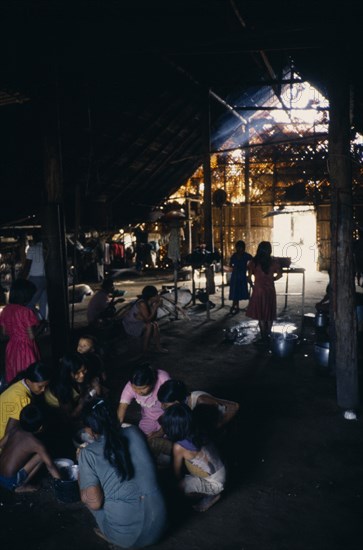 COLOMBIA, North West Amazon, Tukano Indigenous People, Makuna maloca or tribal communal home  interior with Makuna Indian families sharing communal meal of fish and casabe/manioc bread  family fireplaces in background.Tukano  Makuna Indian North Western Amazonia maloca American Colombian Columbia Hispanic Indegent Kids Latin America Latino South America Tukano