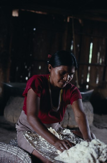 COLOMBIA, North West Amazon, Tukano Indigenous People, Makuna maloca/communal tribal home  interior with woman rubbing down manioc roots on a flint inlain board  to make flour for casabe. Tukano Makuna Indian North Western Amazonia maloca cassava American Colombian Columbia Female Women Girl Lady Hispanic Indegent Latin America Latino South America Tukano