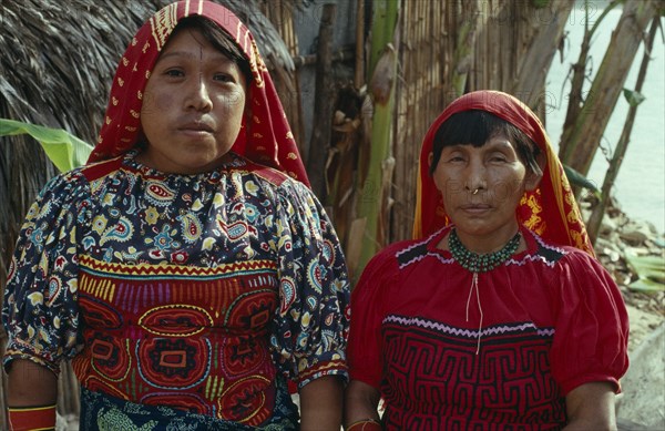 PANAMA, San Blas Islands, Kuna Indians, Head and shoulders portrait of Kuna mother and daughter wearing brightly coloured blouses or dulemola with layered applique mola panels and red and yellow head scarves against strong sun. Cuna Caribbean American Central America Colored Female Woman Girl Lady Hispanic Latin America Latino Panamanian West Indies