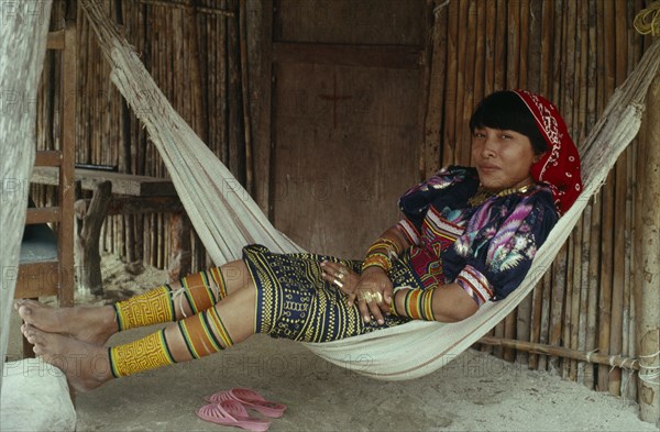 PANAMA, San Blas Islands, Kuna Indians, Young Kuna mother rests in hammock outside home  wearing brightly coloured traditional layered applique mola panel    traditional bead design arm and leg bands and gold nose ring. Cuna Caribbean American Central America Classic Classical Colored Female Women Girl Lady Hispanic Historical Latin America Latino Older Panamanian West Indies