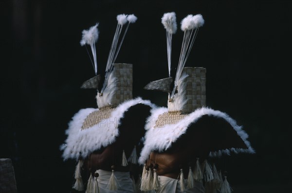PACIFIC ISLANDS, French Polynesia, Tahiti, Two figures dressed in costume with woven mask and cape trimmed with white feathers for re-enactment of an ancient Tahitian coronation performed at a marae or sacrificial altar as part of Bastille Day celebrations.
