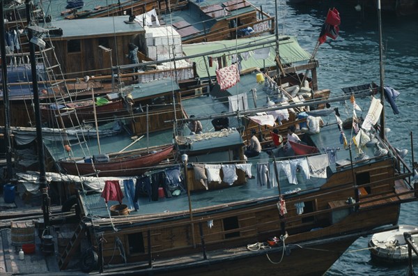 HONG KONG, Aberdeen Harbour, Sampan homes anchored in the harbour.  People and belongings on decks hung with washing.  Fish drying on roof of boat in foreground.