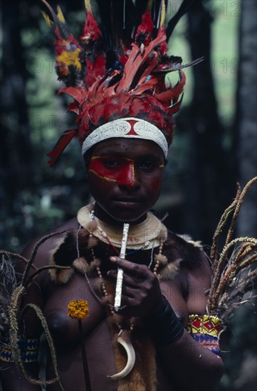 PAPUA NEW GUINEA, People, "Portrait of woman wearing traditional dress and jewellery, elaborate red feather head-dress with band of white beads across forehead and  bead armlets, necklaces and fur collar and red face paint extending down nose and across one eye.  Smoking long cigarette wrapped with newspaper."