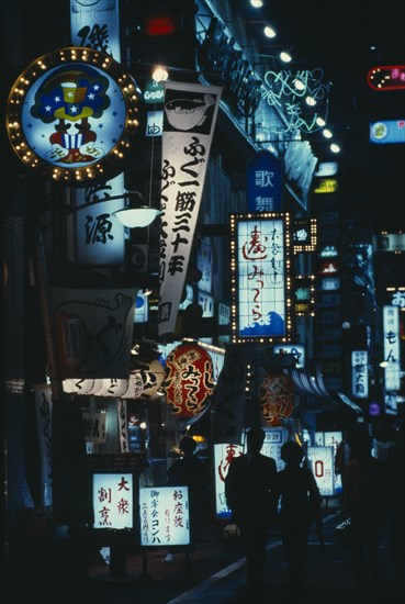 JAPAN, Honshu, Tokyo, "City street scene at night with illuminated neon signs advertising bars, restaurants and other entertainments.  Couple walking in picture centre."