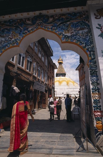 NEPAL, Kathmandu, A woman wearing a red sari walking through ornate Gateway towards Bodhnath Buddhist Stupa.