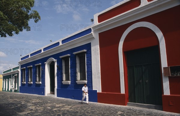 VENEZUELA,  Bolivar State, Ciudad, "Red, blue and white painted house frontages near Plaza Bolivar with a person walking past"