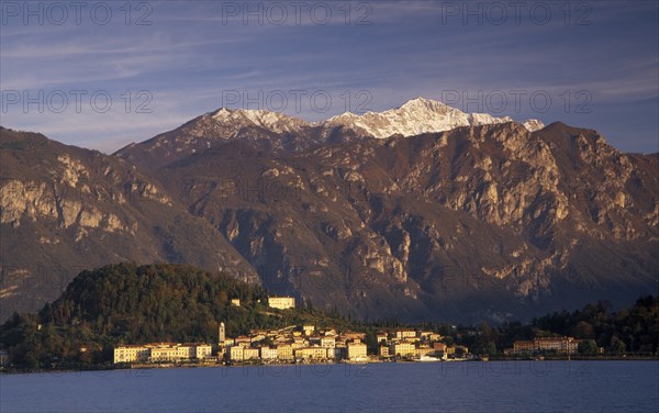 ITALY, Lombardy, Lake Como, Ballagio.  View across Lake Como towards distant town of Ballagio situated at foot of tree covered hillside with mountain backdrop.