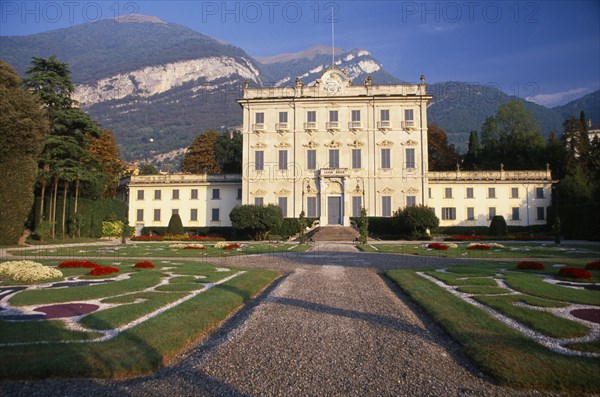 ITALY, Lombardy, Lake Como, "Private villa and formal gardens near Tremezzo, gravel drive leading to entrance steps and lawns inlaid with stone patterns.  Mountains behind."