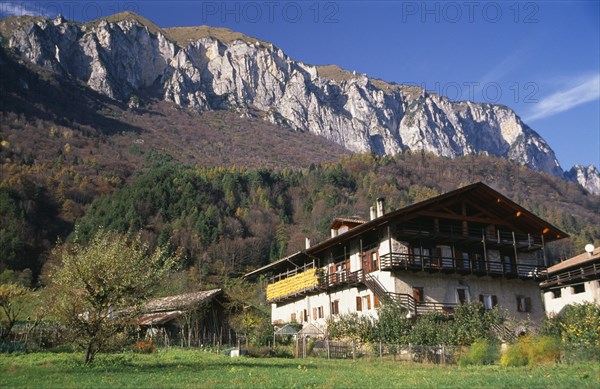 ITALY, Trentino-Alto Adige, Lake Garda Area, "Alpine farmstead near Lago di Tenno.  Traditional building with over hanging roof and balcony, outbuildings and mountain backdrop."