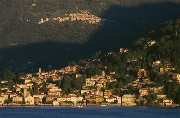 ITALY, Lombardy, Lake Como, Torno.  View across Lake Como towards town spread across hillside in golden sunlight.