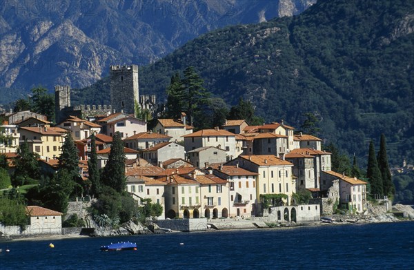 ITALY, Lombardy, Lake Como, Rezzonico.  View across lake to red tiled rooftops of village houses with castle tower and walls behind.
