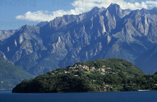 ITALY, Lombardy, Lake Como, View across lake towards distant tree covered peninsula and the Abbey of Piona with mountain backdrop.