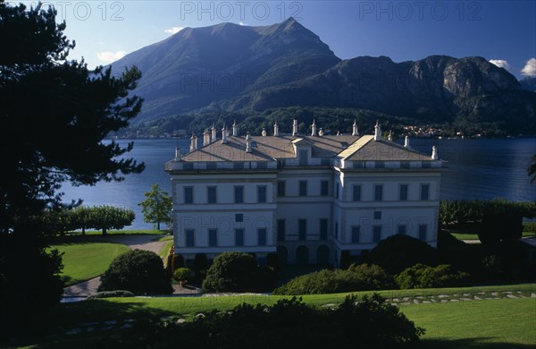 ITALY, Lombardy, Lake Como, Bellagio.  Neo-classical exterior of the Villa Melzi built by architect Giocondo Albertolli 1808-10 as a Summer residence for Francesio Melzi.  Lake and mountains behind