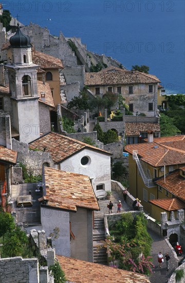ITALY, Lombardy, Lake Garda , "Limone Sur Garda.  View over raised streets, church bell tower and tiled rooftops of houses with tourist vistors.  Lake partly seen beyond."