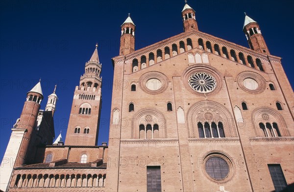ITALY, Lombardy, Cremona, Piazza del Comune.  Southside exterior of the Duomo and bell tower or Torrazzo.  Red brick with circular and arched windows and multiple spires.