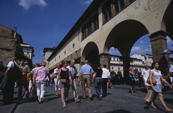 ITALY, Tuscany, Florence, Ponte Vecchio Bridge with visitors walking along street lined with shops and stalls by the bridge arches