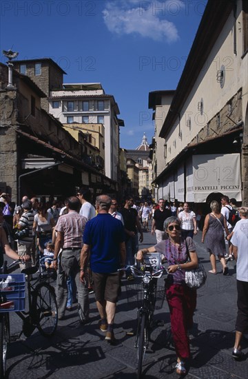 ITALY, Tuscany, Florence, Ponte Vecchio Bridge. People walking along street lined with shops and stalls next to the bridge.