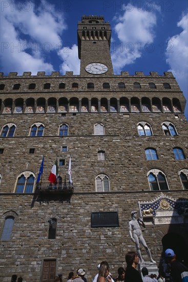 ITALY, Tuscany, Florence, Piazza della Signoria. Palazzo Vecchio entrance and bell tower with a replica of the statue of David by Michelangelo Tourists gathered around the base.