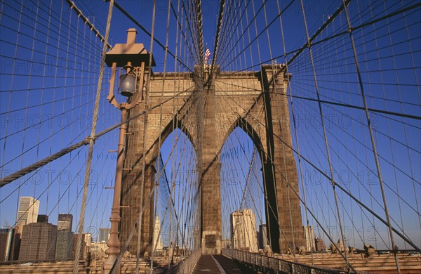 USA, New York, New York City, Brooklyn Bridge.  View across bridge towards Manhattan skyline part framed by central stone tower and intersected by steel wires and suspension cables. Spans the East River.  Construction began in 1870 and the bridge opened for use in 1883.