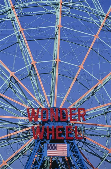 USA, New York, New York City, Coney Island.  Ferris wheel painted blue and orange with sign in red ‘Wonder Wheel’ and American Stars and Stripes flag below.  Cropped to fill frame.