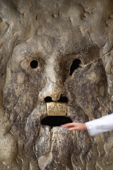 ITALY, Lazio, Rome, The 2nd Century BC drain cover Bocca della Verite or Mouth of Truth mounted ona wall at the Church of Santa Maria in Cosmedin. A female hand is pulled away from the mouth where tradition has it the jaws will close over the hands of those who tell a lie