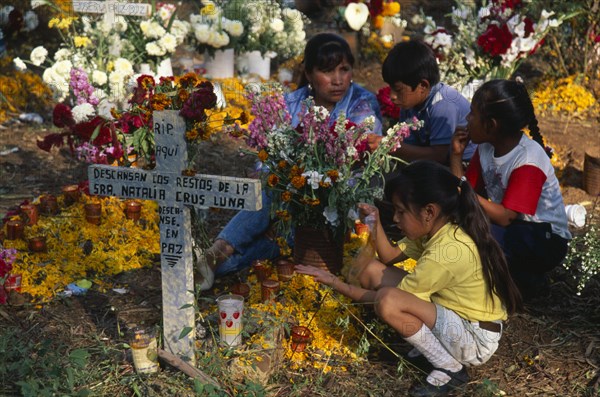 MEXICO, Michoacan, Patzcuaro, Tzurumutaro Cemetery.  Children by family grave decorated with candles and flowers for the Day of the Dead.