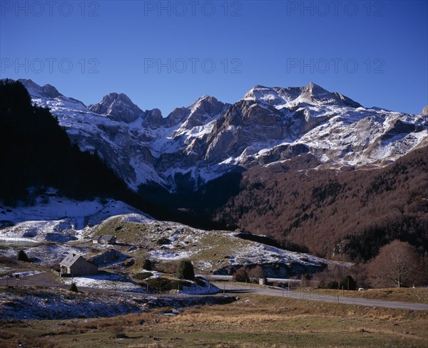 FRANCE, Aquitaine, Pyrenees Atlantiques, Winter view west from village of Peyrenere near mountain pass of Col du Somport towards Sierra de Bernera in light snow with two stone houses and road in foreground.