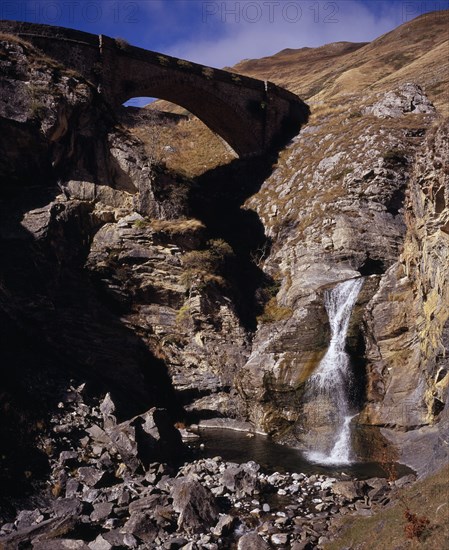 FRANCE, Aquitaine, Pyrenees Atlantiques, Defile de Tourmont.  Gave de Brousset waterfall flowing from rocks into pool below with arched bridge above.