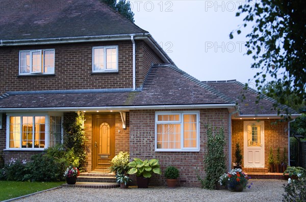 ARCHITECTURE, Buildings, Homes, Semi detached house brick built and garden with gravel driveway at dusk with lights on in windows and above external doors