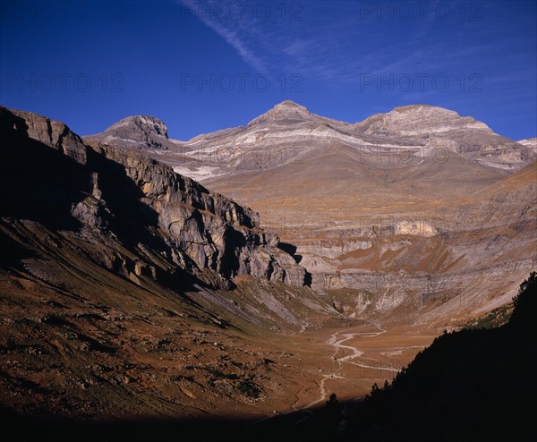 SPAIN, Aragon, Valle de Ordesa, View at north east end of valley towards mountains of Las Tres Sorores and peak of Monte Pedido (3355m).  Trees in foreground and clearly visible coloured rock strata.
