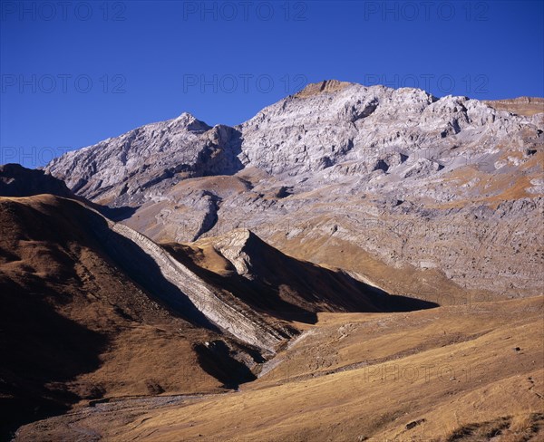 SPAIN, Aragon, Pyrenees, "Sierra de Tendenera and highest point Pico de Tendener.  Peaks from left to right, 2823 - 2853 m.  Grey, eroded rock and scree with golden brown grass covering lower slopes"