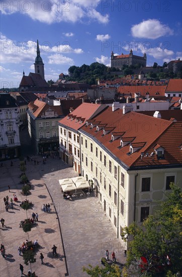 SLOVAKIA, Bratislava, "View over paved square and cafe, across red tiled rooftops of the Old Town towards Cathedral of St Martin and Bratislava Castle."
