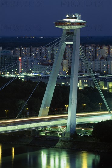 SLOVAKIA, Bratislava, Novy Most (New Bridge) topped with restaurant over the River Danube with views towards Petrzalka tower blocks at night with light trails from passing traffic below.