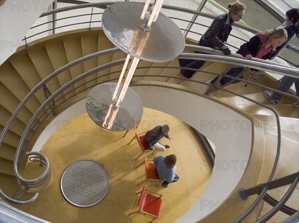 ENGLAND, East Sussex, Bexhill-on-Sea, The De La Warr Pavilion. Interior view down the helix staircase with chrome Bauhaus globe lamps. Visitors walking the stairs and people sitting on chairs seen at the bottom