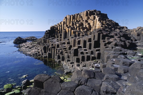 NORTHERN IRELAND, Co Antrim, Giants Causeway, Interlocking basalt stone columns left by volcanic eruptions. View across the main and most  visited section of the causeway with the coastline seen behind.