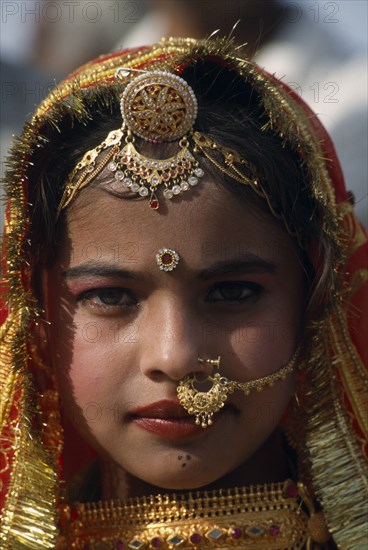 INDIA, Rajasthan, Jaisalmer, Head and shoulders portrait of a young girl wearing traditional jewellery at the Desert Festival