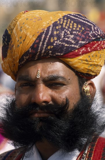 INDIA, Rajasthan, Jaisalmer, Head and shoulders portrait of a Mr Desert contestant with a beard wearing a colourful turban at the Desert Festival