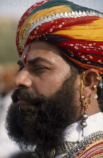 INDIA, Rajasthan, Jaisalmer, Head and shoulders side profile portrait of a Mr Desert contestant with a beard wearing a colourful turban and traditional earrings at the Desert Festival