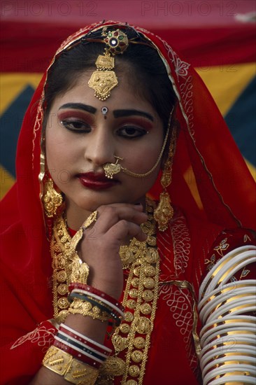 INDIA, Rajasthan, Jaisalmer, Portrait of a Miss Desert contestant wearing red with traditional jewellery at the Desert Festival