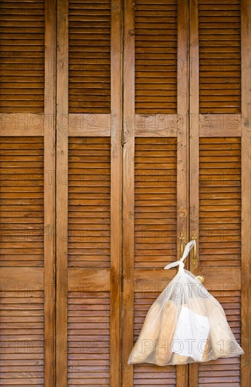 MALTA, Saint Julians, Plastic bag containing loaves of fresh bread tied to the handle of wooden louvre shutter doors