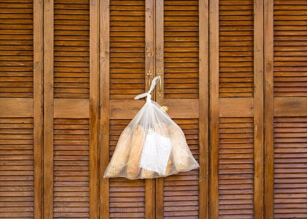MALTA, Saint Julians, Plastic bag containing loaves of fresh bread tied to the handle of wooden louvre shutter doors