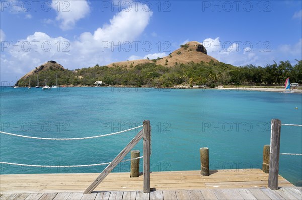 WEST INDIES, St Lucia, Gros Islet , Pigeon Island National Historic Park seen from a nearby wooden jetty with yachts at anchor in Rodney Bay